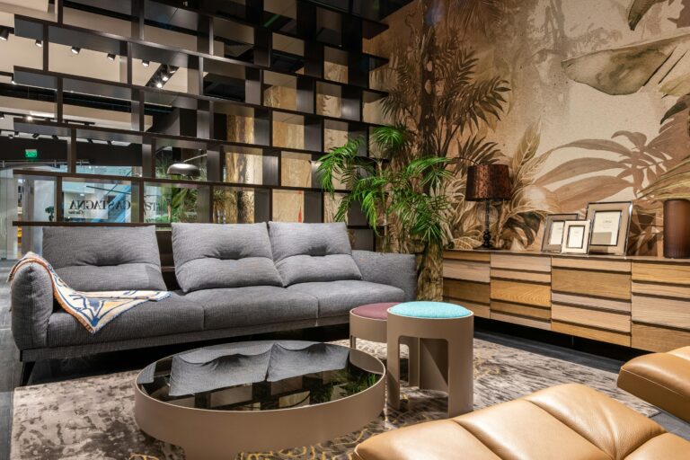 Stylish living room featuring a plush sofa, mirrored table, and tropical-themed wallpaper.